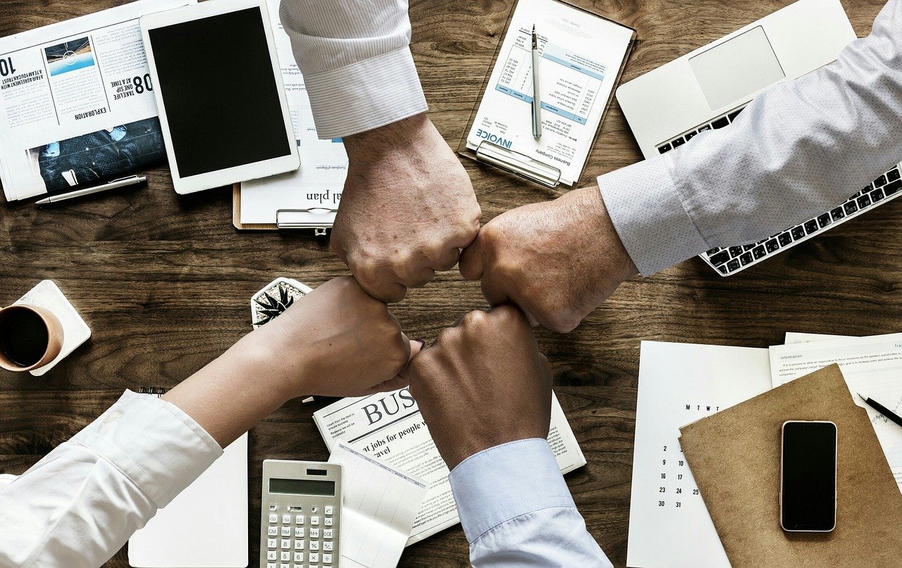 Colleagues joining fists over a desk covered with laptops and papers